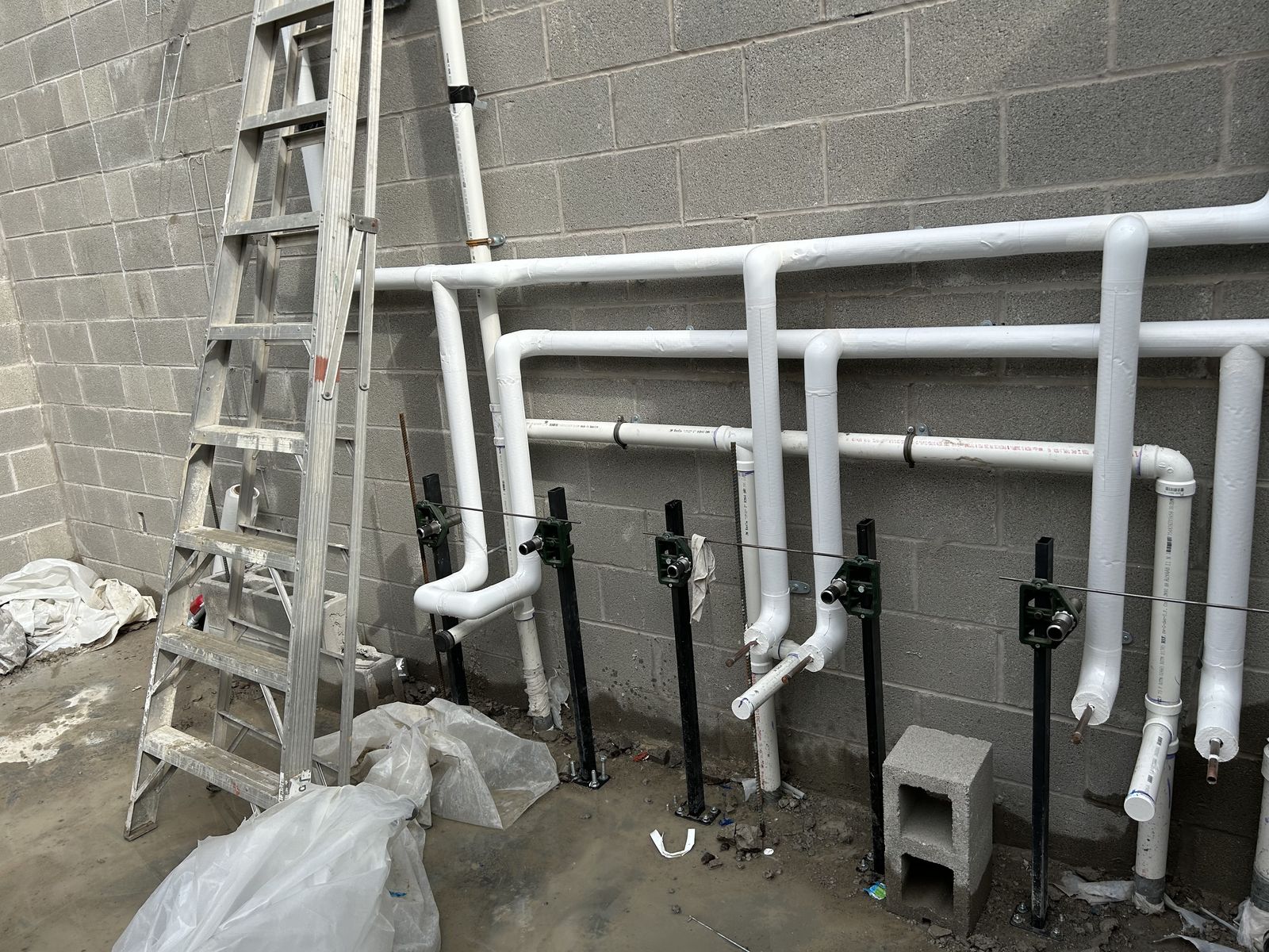 Commercial PVC waste and vent stacks mounted on adjustable stands against a block wall