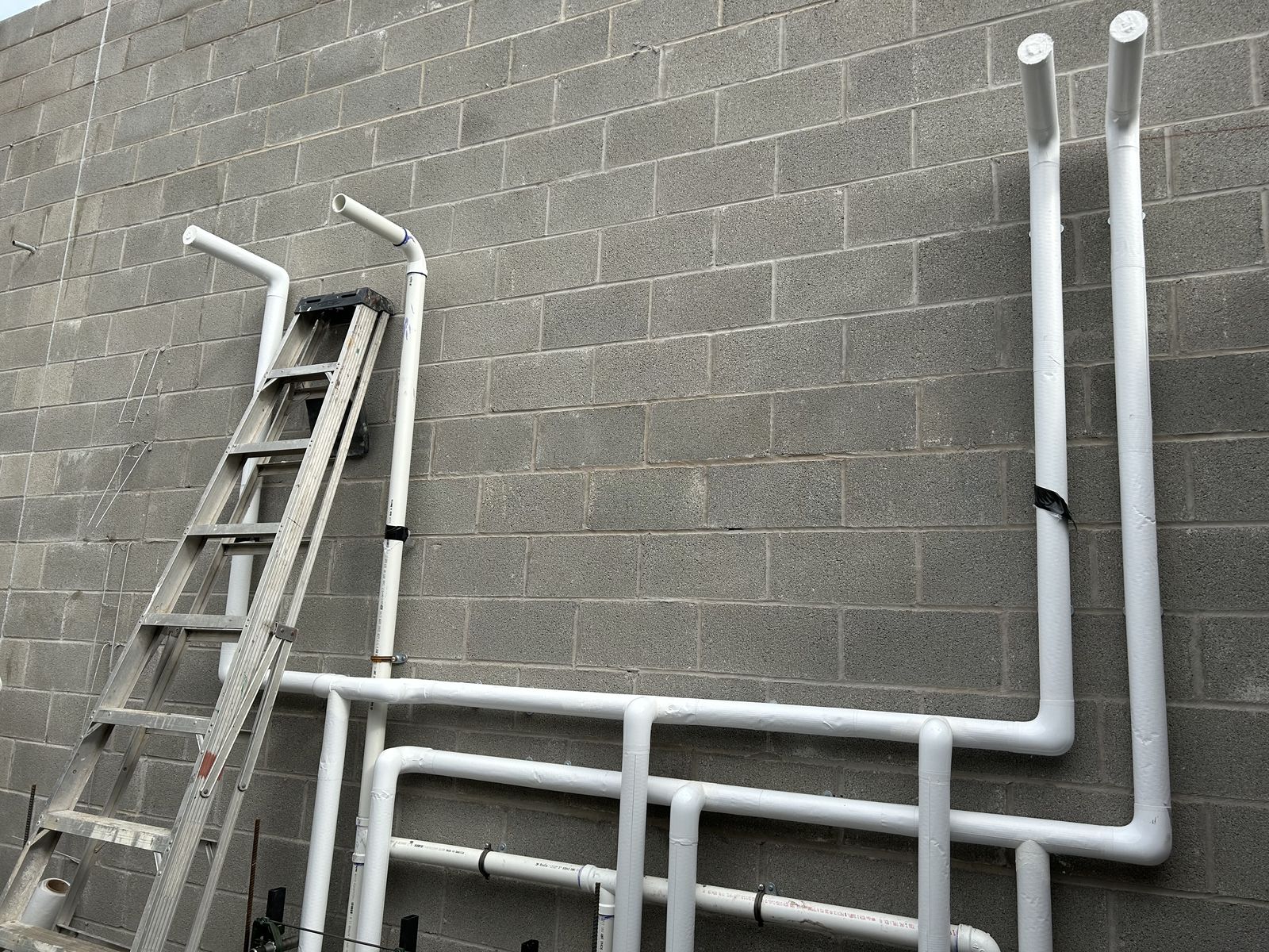 Exterior cinder-block wall with neatly routed white PVC waste and vent risers