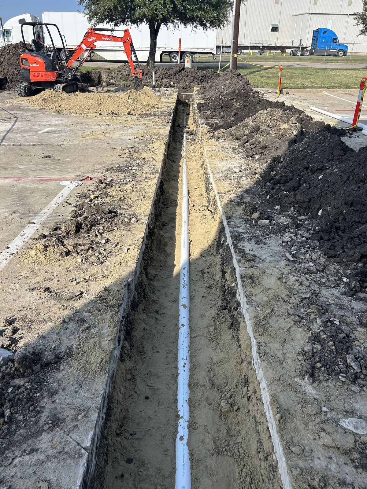 Long utility trench across a commercial parking lot with a mini-excavator and pipe run