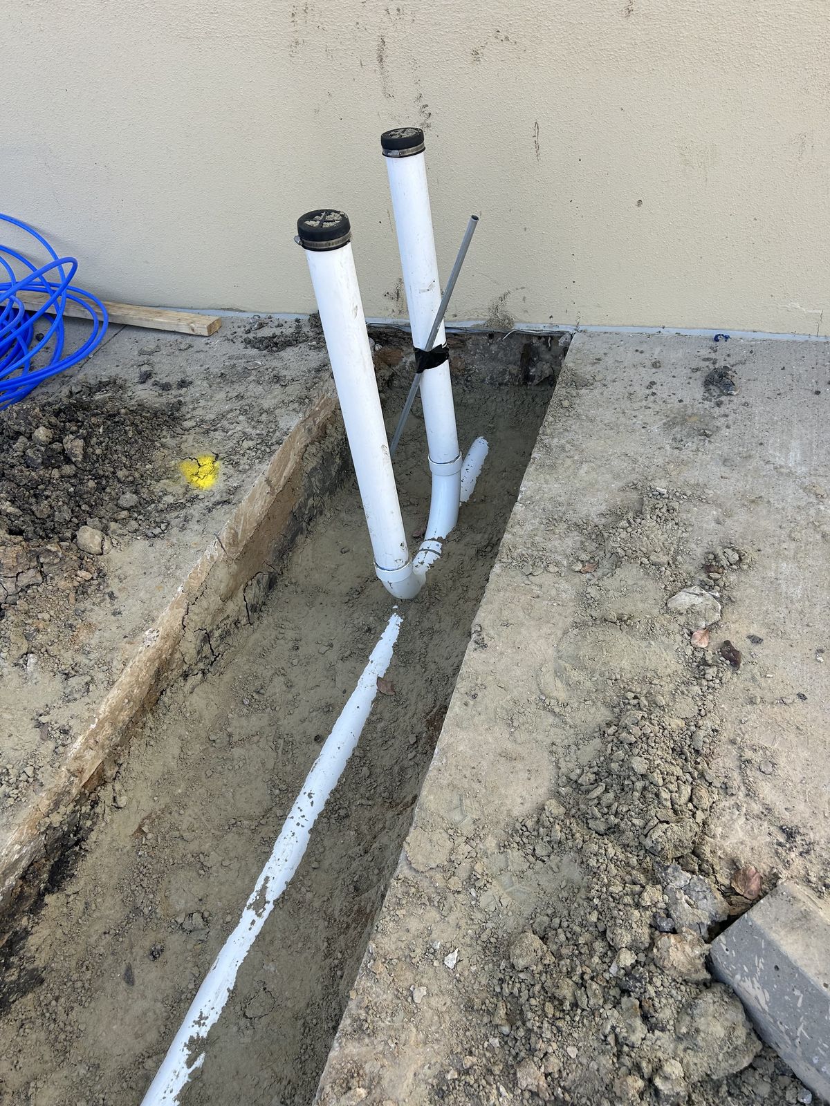 Exterior sewer cleanout risers installed in a trench along a building foundation