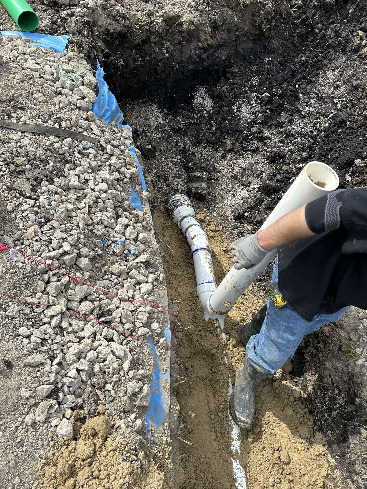 Hauser Plumbing installer setting and gluing PVC sewer pipe in a gravel-bedded trench