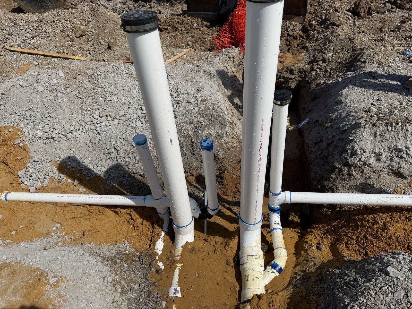 Close-up detail of a PVC drain stub-up manifold in sandy soil at a commercial site