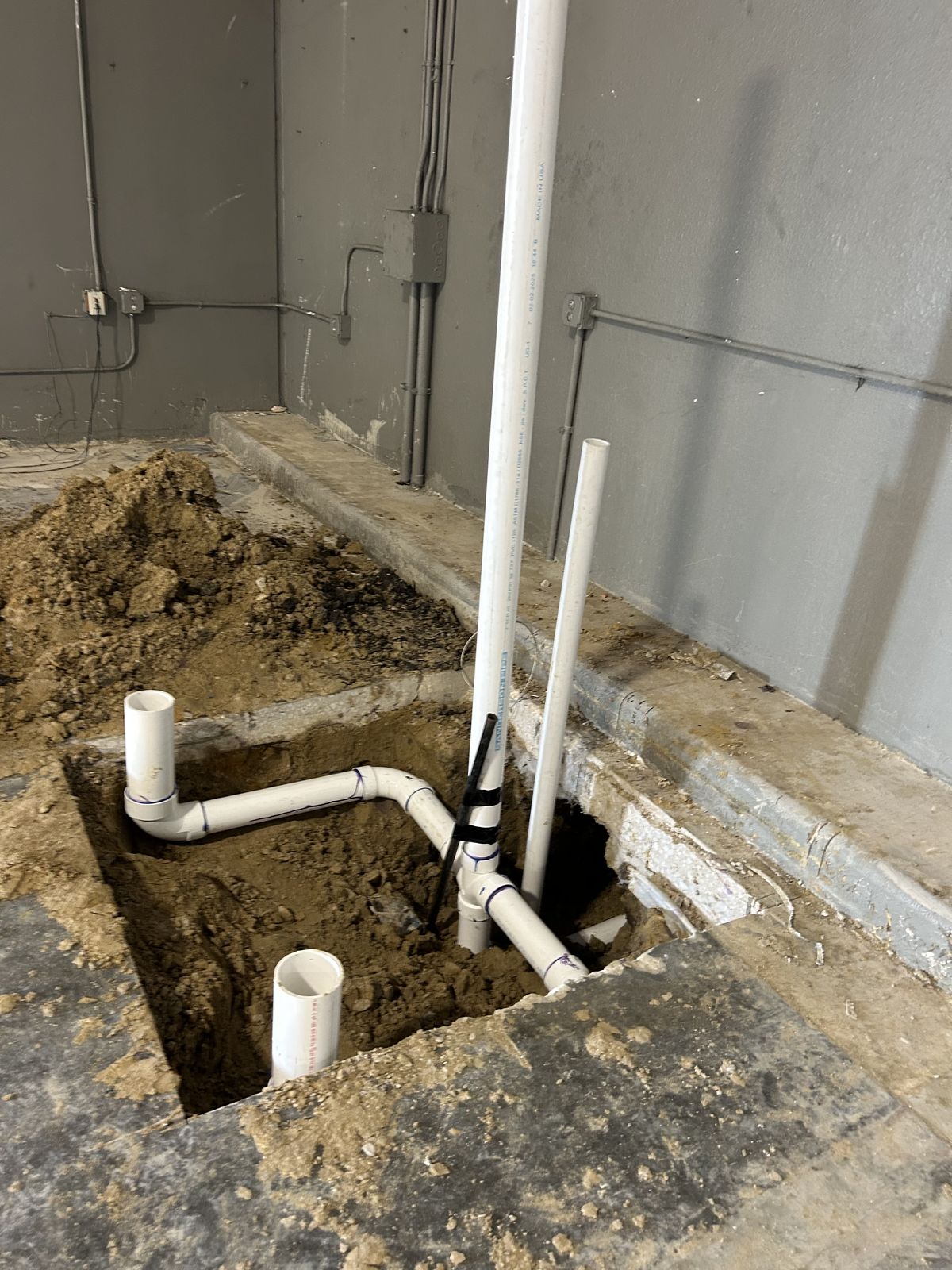 Interior under-slab plumbing rough-in cut into a concrete floor for a commercial renovation